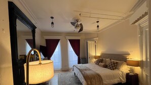 A bedroom with a bed, a lamp, a mirror, a ceiling fan, and a window with curtains. - Peaceful 1-bedroom suite in boutique guesthouse with AC in vibrant New York (New York)