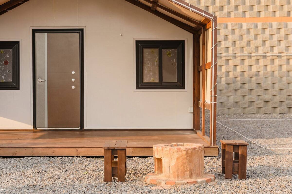 A small, single-story building with a wooden deck, a door, and two windows.