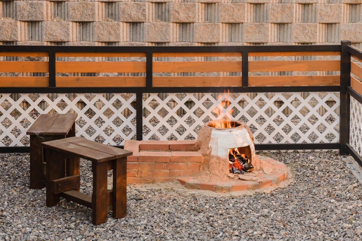 A patio with a brick fire pit, wooden furniture, and a white lattice fence.