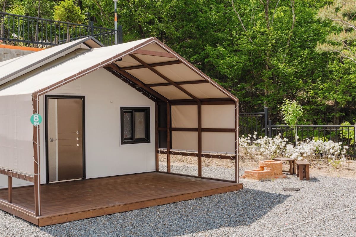 A small, single-story building with a wooden deck, a door, and a window.
