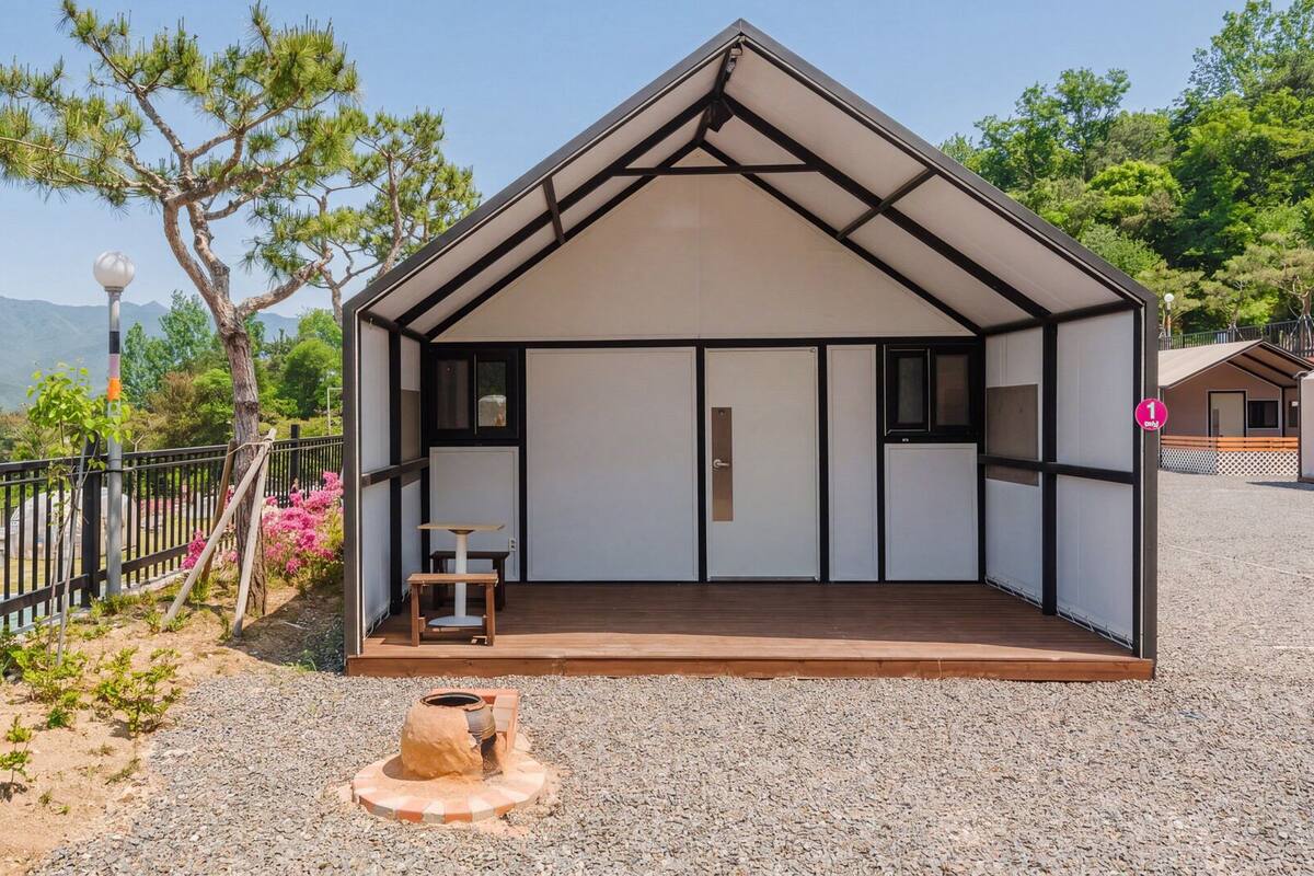 A small, single-room cabin with a sloped roof, a wooden deck, and a gravel ground.