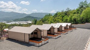 A row of modern, single-story cabins with balconies, set against a backdrop of mountains and a clear sky. - Pocheon Youngyoung Glamping (Pocheon)