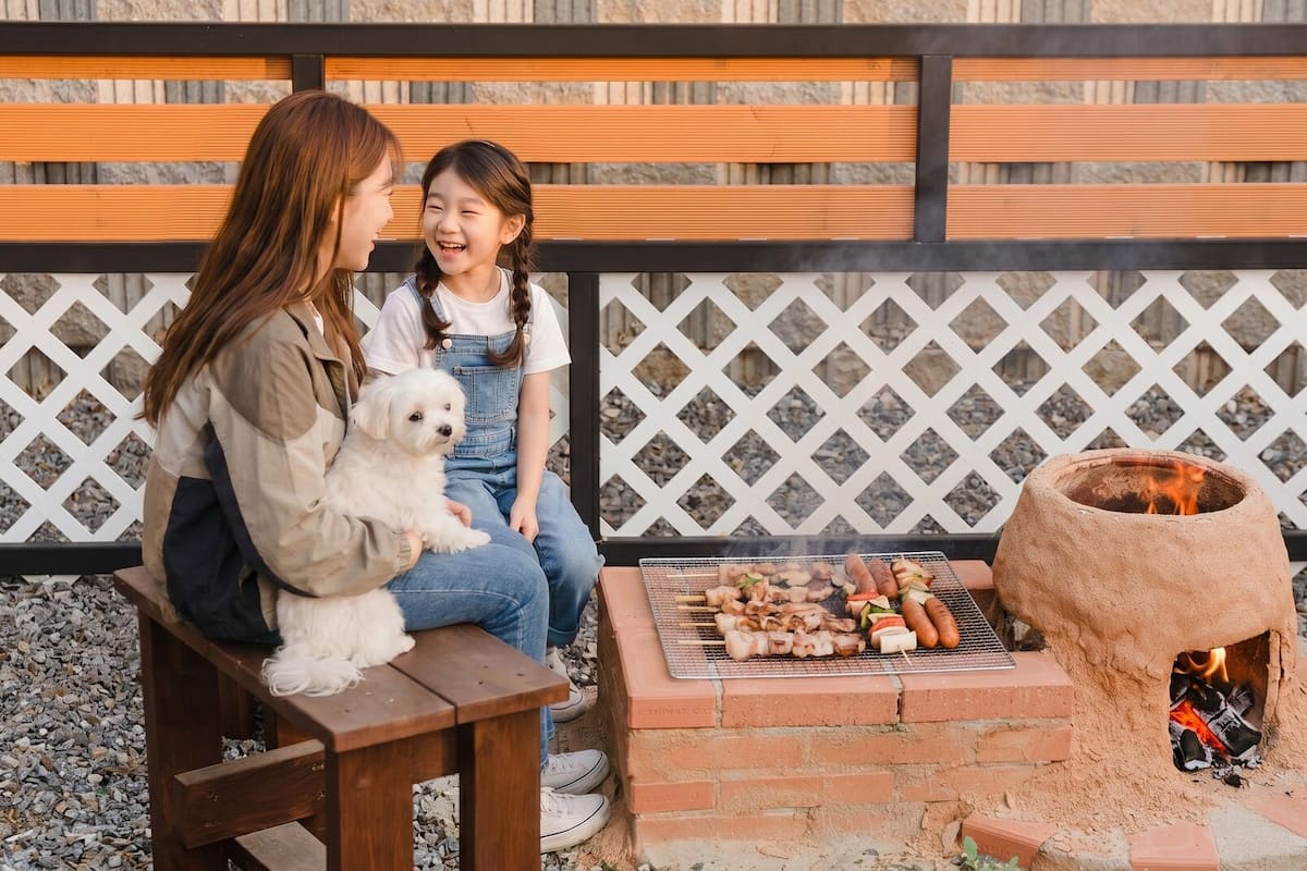 A wooden bench, a small brick grill with food, and a stone oven.