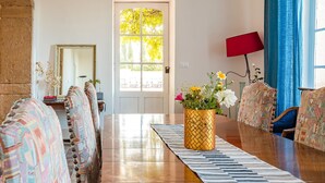 A dining area with a long table, patterned chairs, a vase with flowers, and a view through a window. - Château avec piscine privée (Valréas)