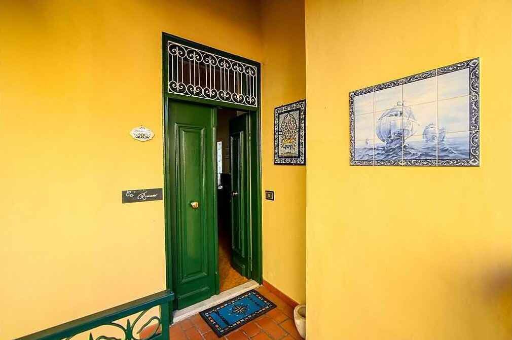 Um corredor com porta verde, parede revestida de azulejos com pintura náutica e pequeno azulejo decorativo acima da porta.