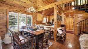 Interno di una baita in legno con zona pranzo, angolo cottura e scala.