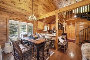 A wooden cabin interior with a dining area, kitchen, and staircase.