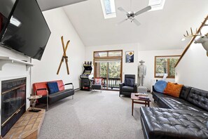 Una sala de estar con chimenea, televisor, ventilador de techo, ventana grande y una estatua.