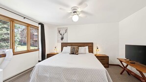 Ein Schlafzimmer mit einem Bett, einem Deckenventilator, einem Fernseher und einem Fenster.