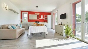 Una sala de estar moderna con sofá, mesa de comedor y cocina al fondo.