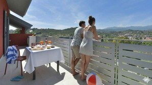 Un balcón con una mesa lista para comer, una pelota de playa y vistas a un pueblo y colinas.