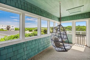 Ein Zimmer mit Hängesessel, großen Fenstern und Blick auf Grünflächen und ein Gebäude.