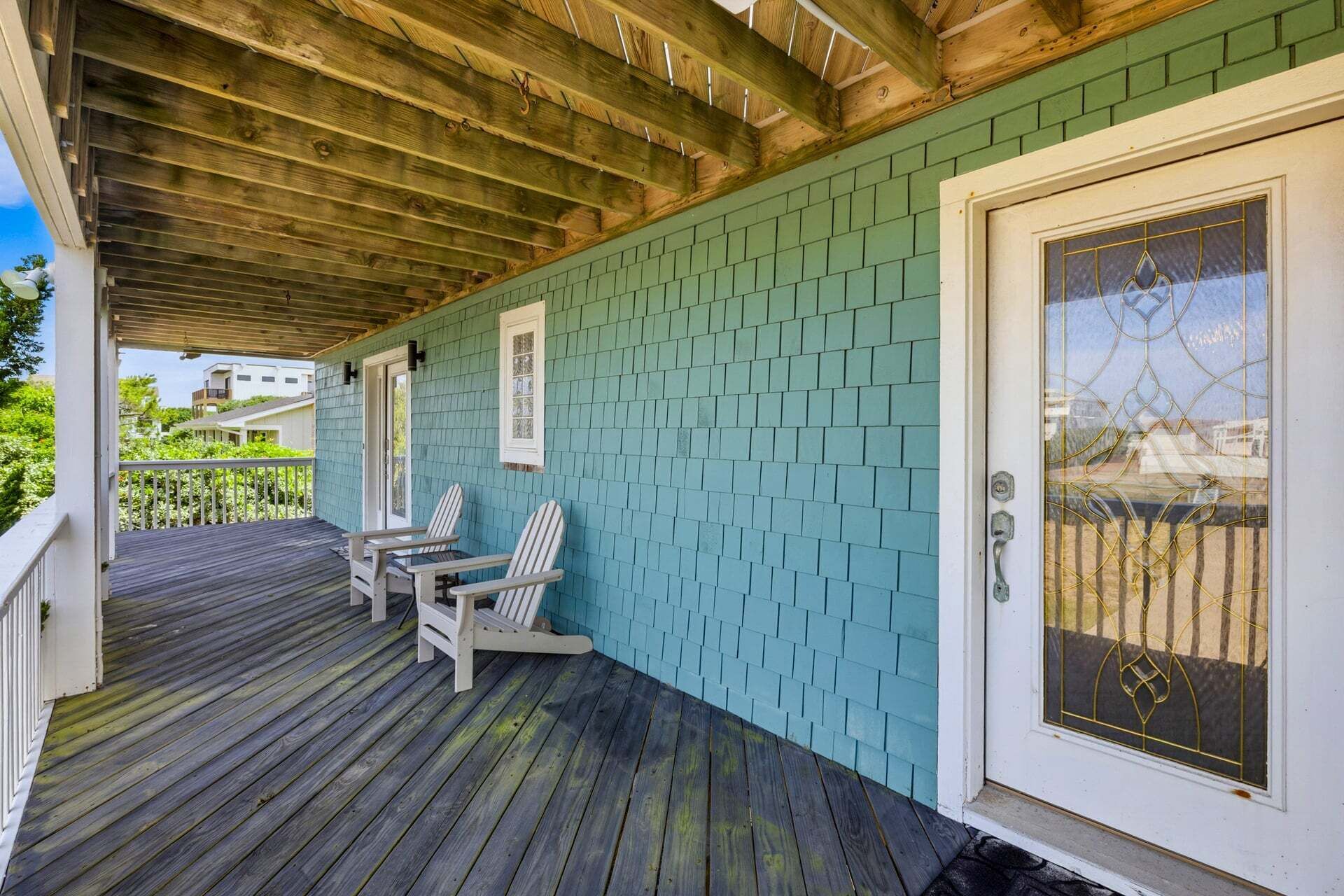 Un portico riparato con soffitto in legno, parete color acquamarina e porta bianca con un pannello di vetro.
