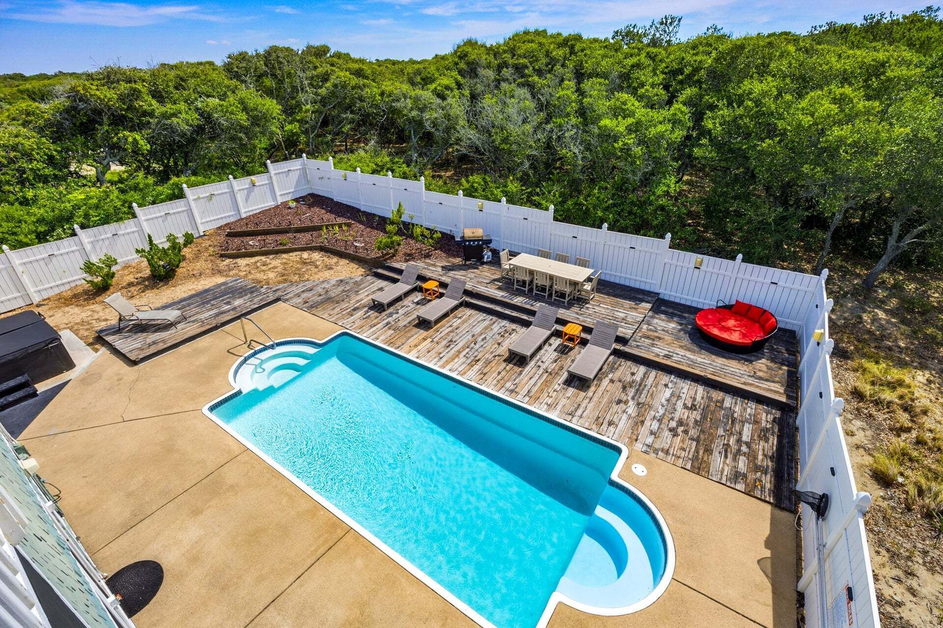 A backyard with a swimming pool, deck chairs, a barbecue grill, and a wooden deck.