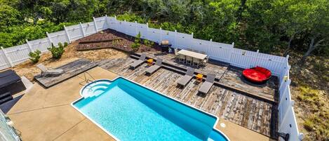 A backyard with a swimming pool, deck chairs, a barbecue grill, and a wooden deck.