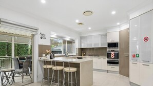Een moderne keuken met een bar, witte kastjes, roestvrijstalen apparatuur en uitzicht op groen.