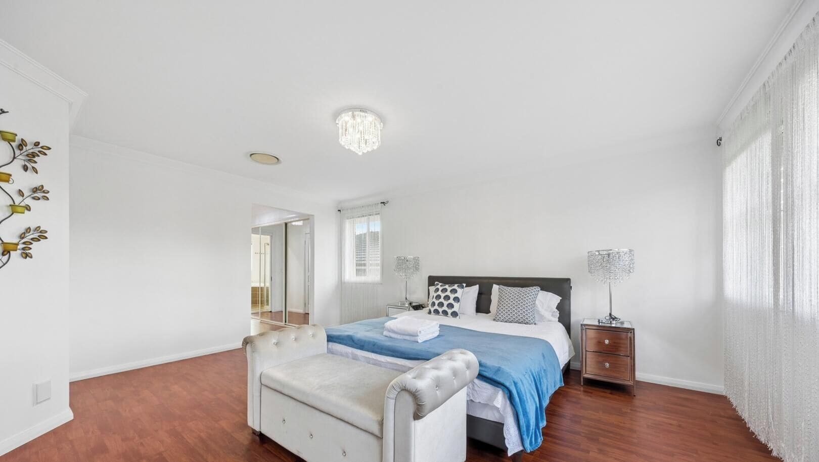 A bedroom with a bed, bedside tables, a chair, a mirror, and a chandelier.