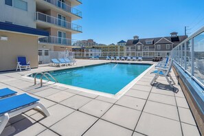 Piscina com espreguiçadeiras, um deck ensolarado e vista para edifícios altos.
