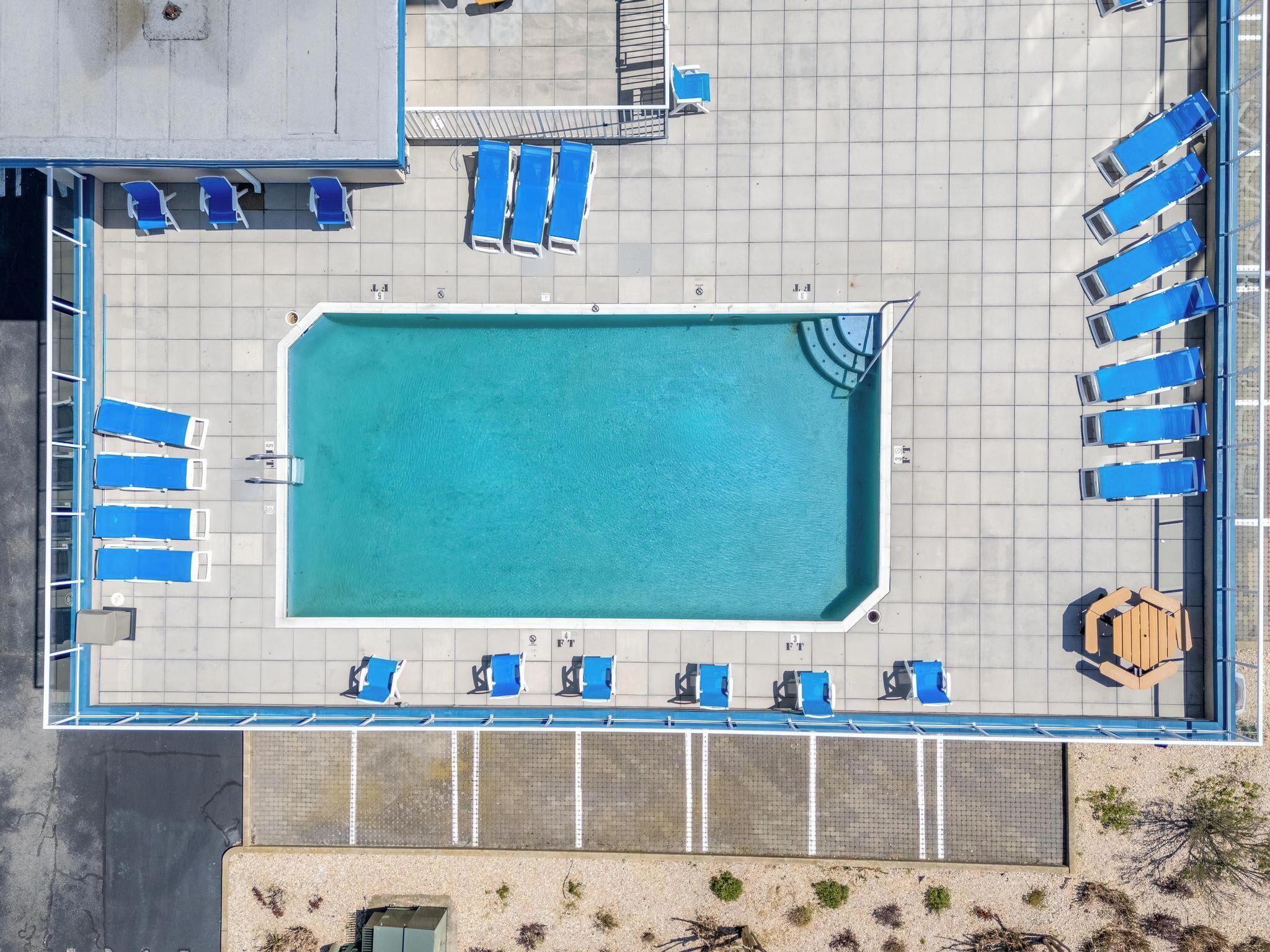 Vista aérea de una piscina con sillas reclinables azules y una zona de terraza de madera.