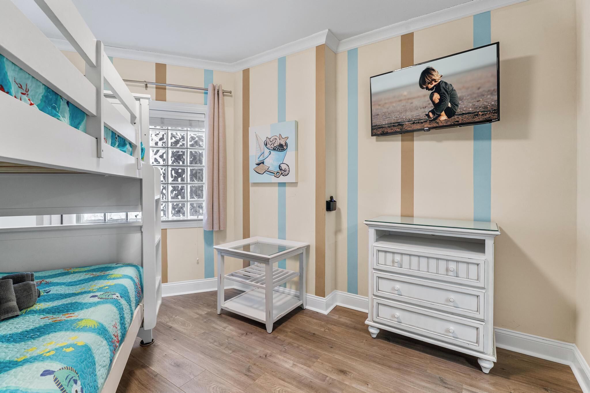 Una habitación con literas, una mesita pequeña, un aparador y un televisor montado en la pared.