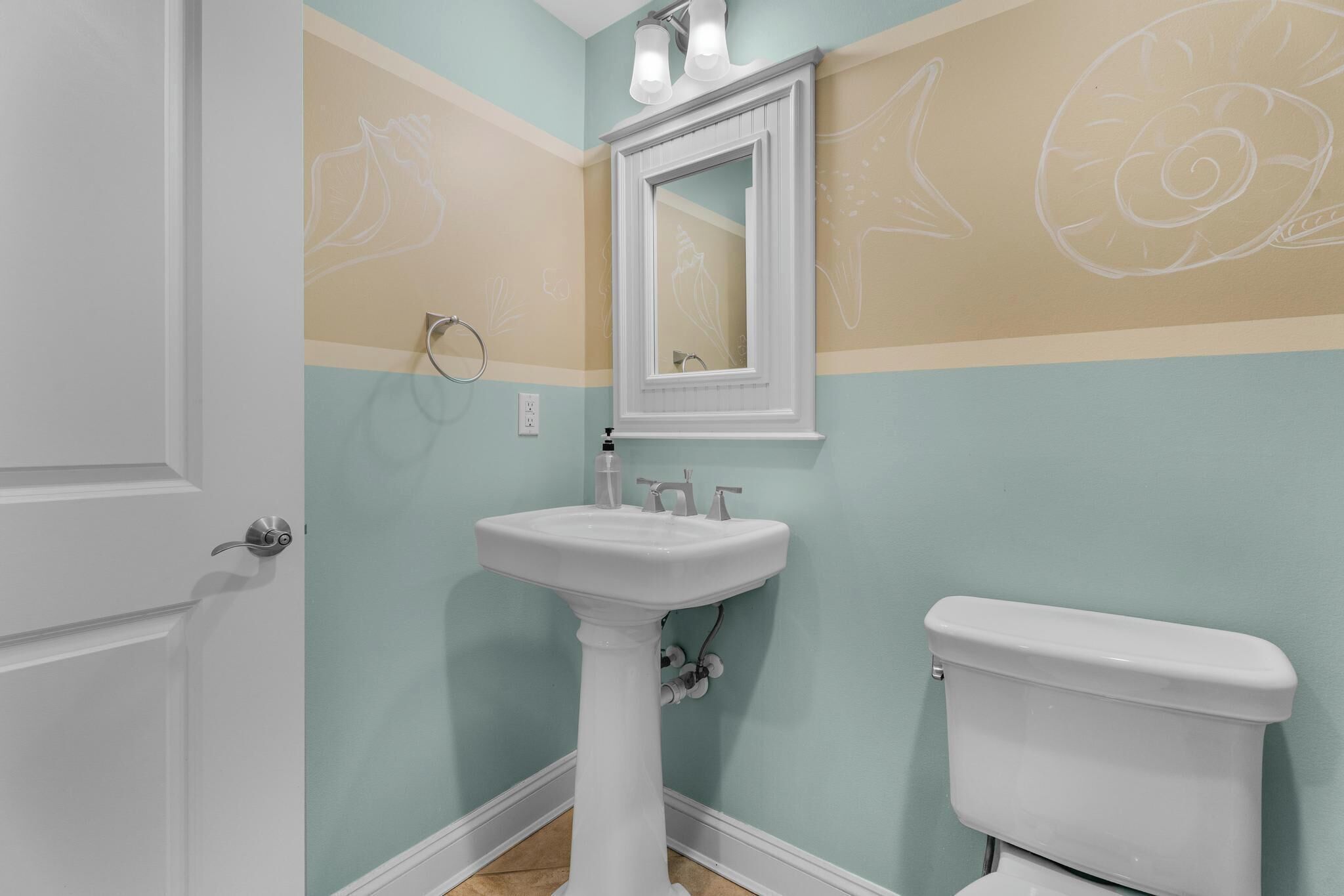 A bathroom with a pedestal sink, a toilet, and a wall-mounted mirror.