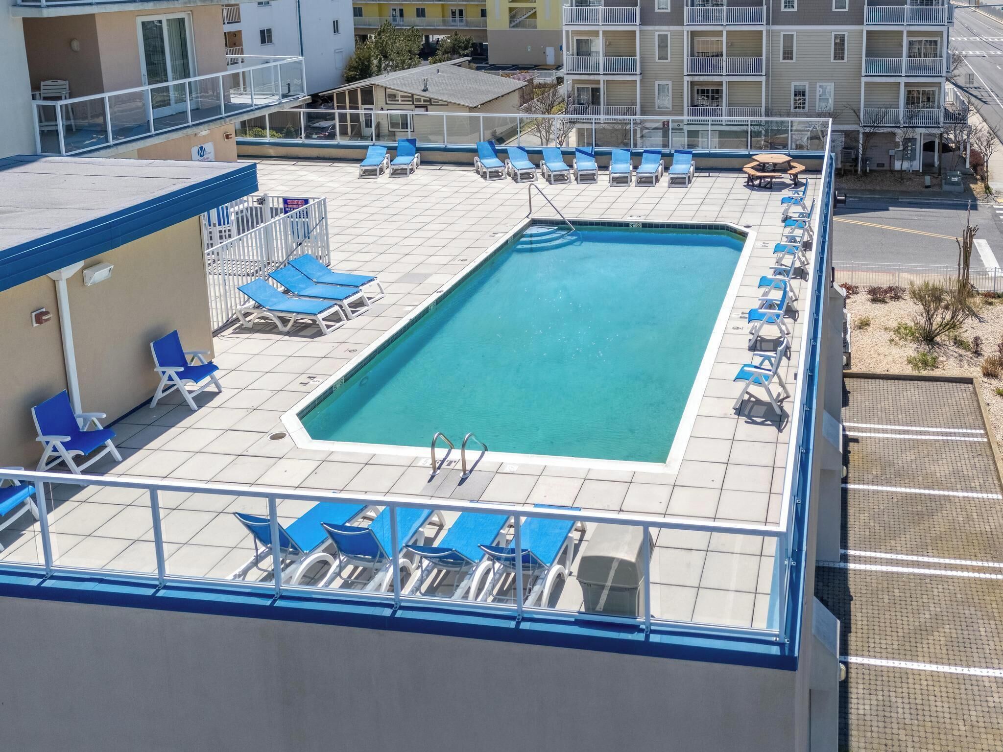 A rooftop pool with blue lounge chairs and a clear blue pool.