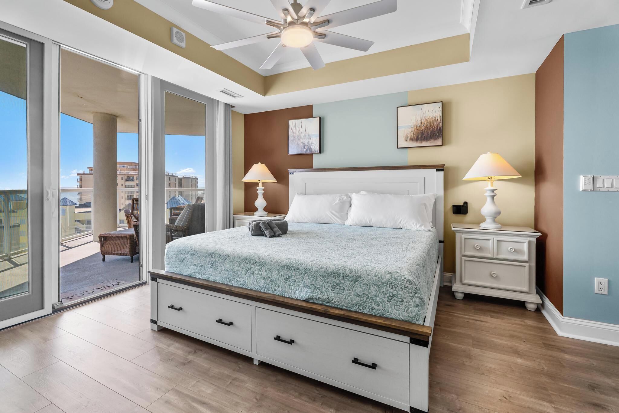 A bedroom with a bed, two bedside tables, a ceiling fan, and a view through a sliding glass door.