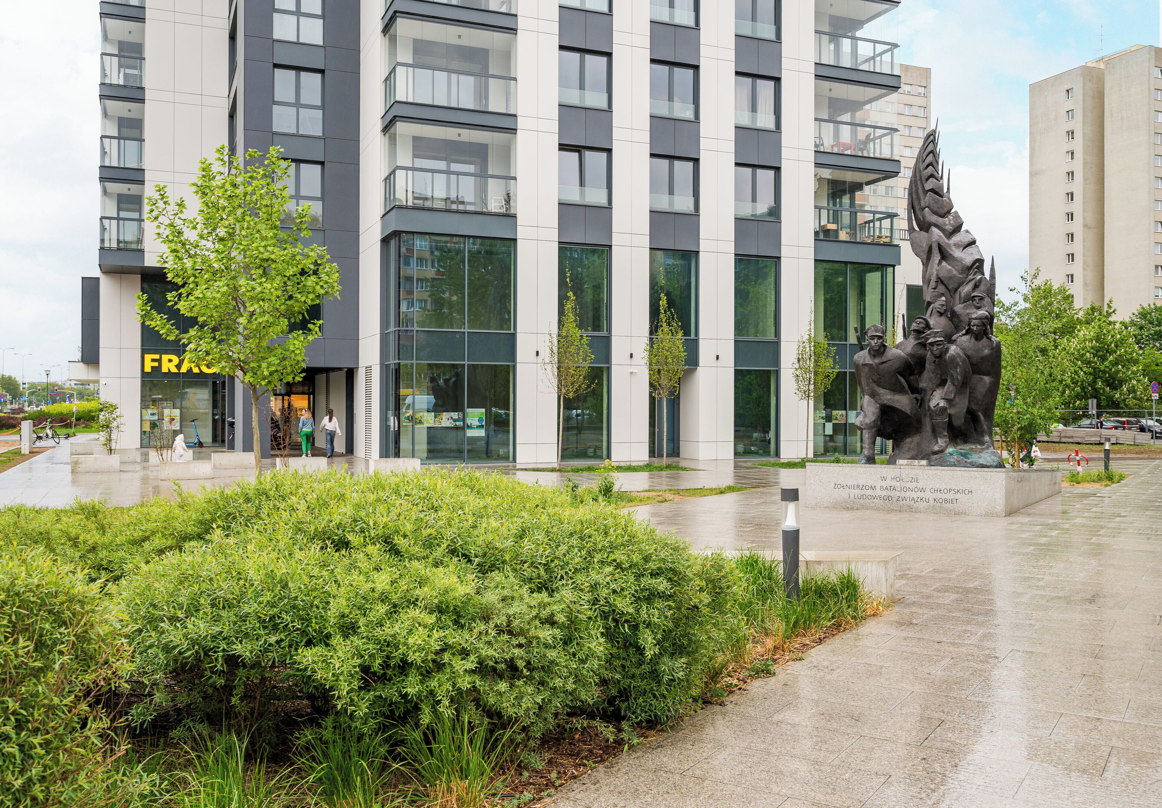 Un edificio moderno con ampie finestre, una statua e un giardino curato.