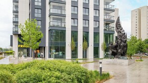 Een modern gebouw met grote ramen, een standbeeld en een verzorgde tuin.