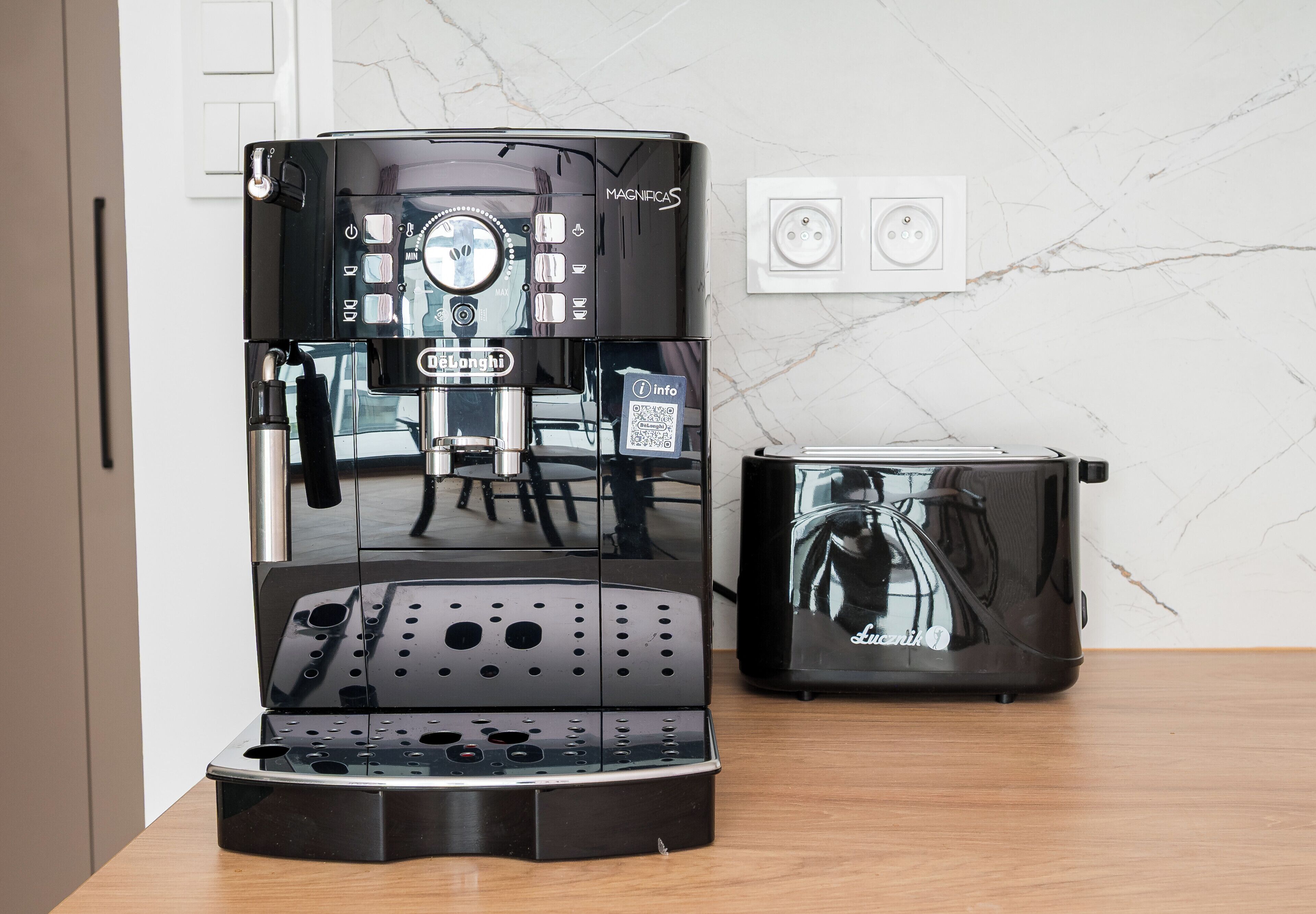 A coffee machine and toaster on a wooden table with a marble wall and electrical outlets in the background.