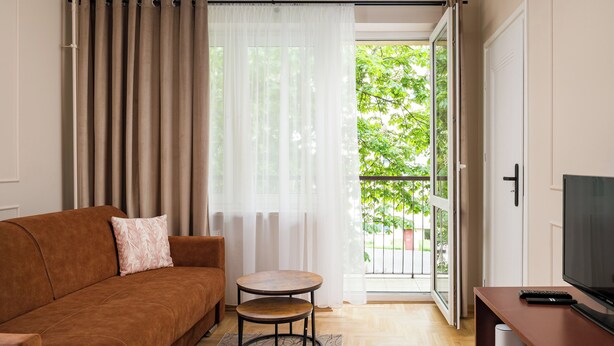 A living room with a sofa, a small round table, a TV stand, and a sliding glass door leading to a balcony. - Aleja Waszyngtona Sowinski Apartment (Warszawa)