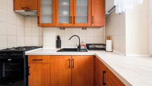 A kitchen with wooden cabinets, a stove, a sink, and a countertop. - Aleja Waszyngtona Sowinski Apartment (Warszawa)