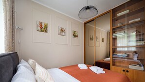 A neatly made bed with a red cover, a grey sofa, and a wooden cabinet with glass doors. - Aleja Waszyngtona Sowinski Apartment (Warszawa)