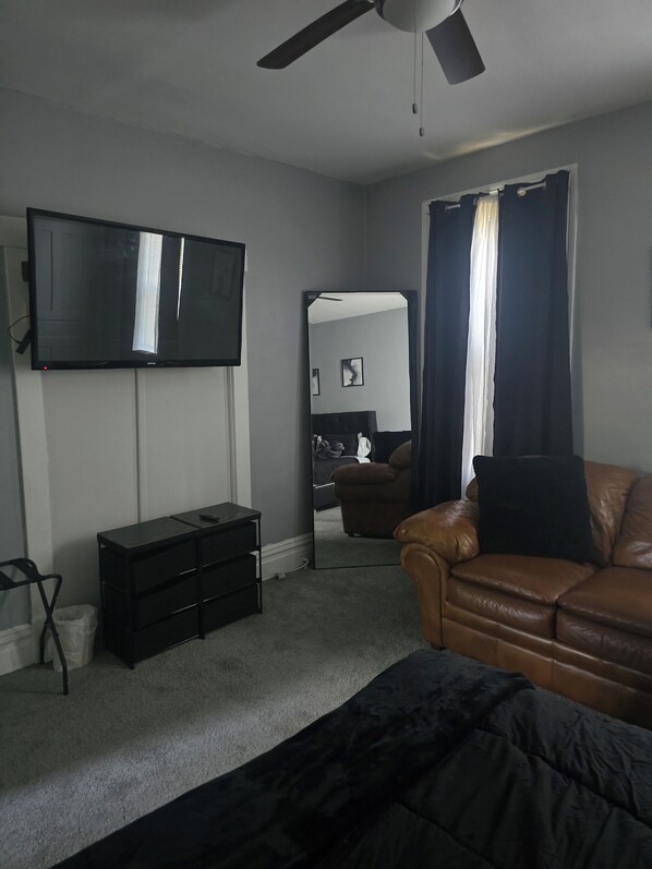 Een woonkamer met een televisie, een bank, een salontafel, een plafondventilator en een grote spiegel.