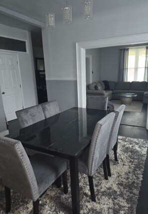 A dining area with a black table and grey upholstered chairs, a grey shaggy rug, and a grey sofa in the background. - Perfect 5-bedroom house in Pittsburgh for your next getaway (Pittsburgh)