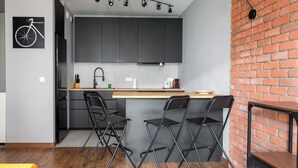 A modern kitchen with grey cabinets, a brick accent wall, and a bicycle artwork. - Żerań Brick Loft Apartment (Warszawa)