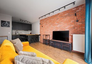 Ett modernt vardagsrum med en tegelvägg, en platt-TV, en soffa och ett köksområde i bakgrunden.