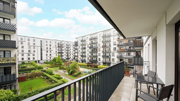 A balcony with a view of a residential complex, a small garden, and a dining area with a table and chairs. - Żerań Brick Loft Apartment (Warszawa)