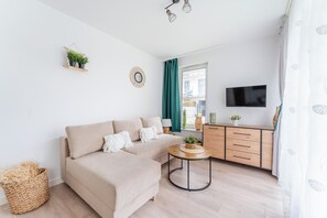A modern living room with a sofa, a small round table, a TV, and a window with curtains. - Rybacka Seaside Apartment (Kołobrzeg)