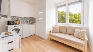 Um espaço compacto com cozinha compacta, máquina de lavar, sofá e janela com vista.