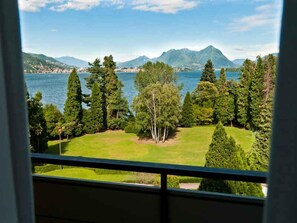 Blick aus einem Fenster auf einen See mit Bergen im Hintergrund und einer gepflegten Rasenfläche.