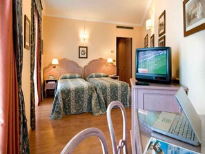 Ein Hotelzimmer mit zwei Betten, einem Fernseher, einem Laptop und einem Schreibtisch mit einem Stuhl.