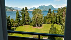 Une vue depuis une fenêtre donnant sur un lac, avec des montagnes en arrière-plan et une pelouse bien entretenue.
