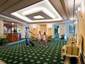 Eine Hotelhalle mit einem grün gemusterten Teppich, einem Empfangstresen und verzierten Möbeln.