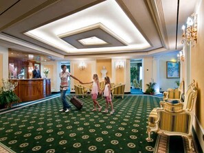 A hotel lobby with a green patterned carpet, a reception desk, and ornate furniture. - Holiday apartment with air conditioning and balcony with lake view (Baveno)