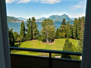 Blick aus einem Fenster auf einen See mit Bergen im Hintergrund und einer gepflegten Rasenfläche.