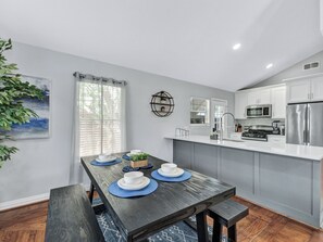 A modern kitchen with white cabinets, stainless steel appliances, and a dining area with a wooden table and blue placemats. - Dallas Getaway w/ Hot Tub, Fire Pit & Detached Suite (Dallas)