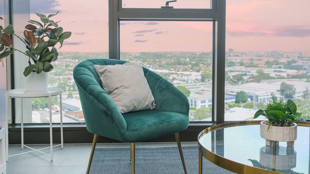 A teal armchair with a cushion, a small round table, and a potted plant on a windowsill.