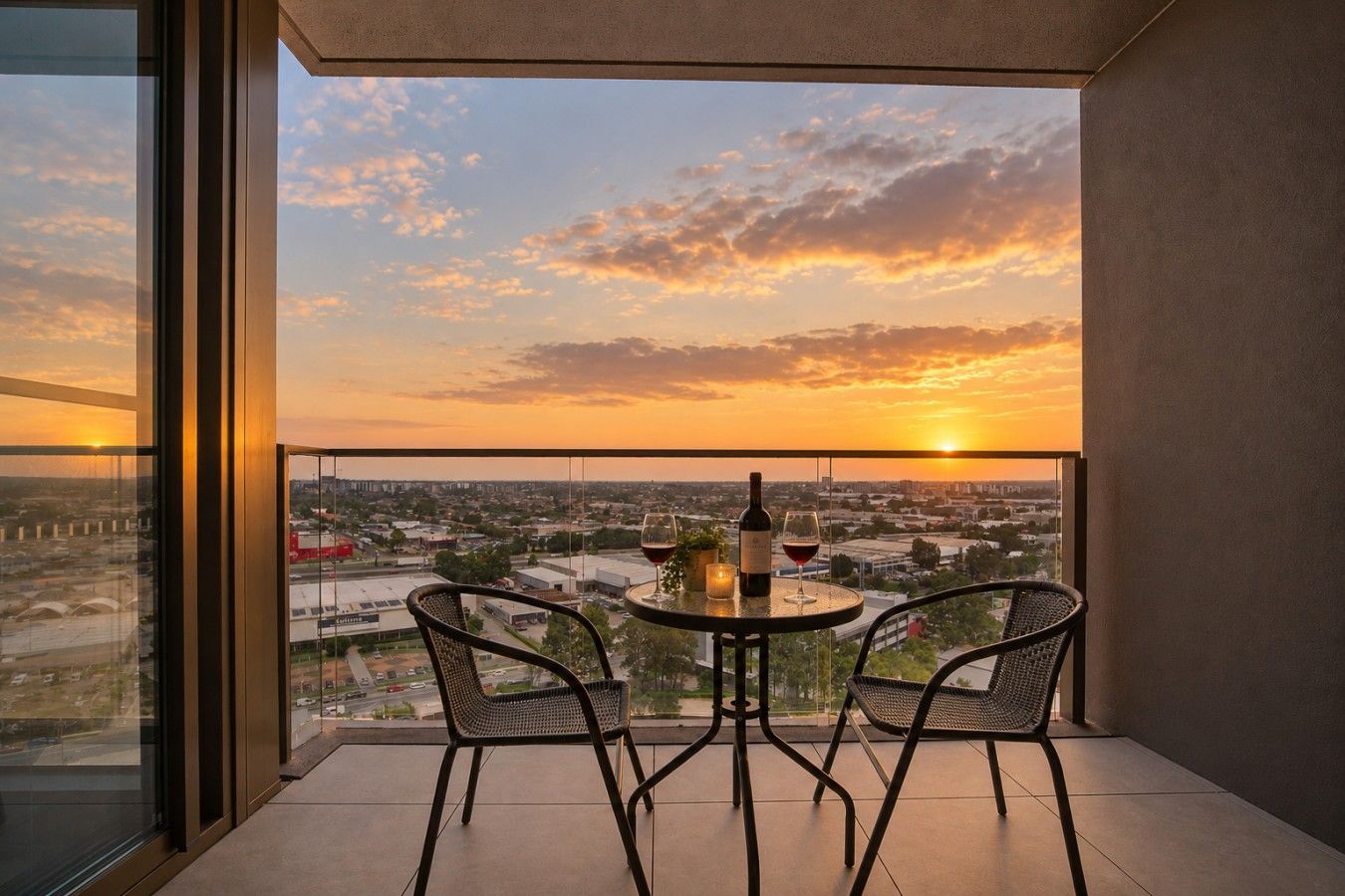 Ein Balkon mit zwei Stühlen und einem Tisch, mit Blick auf eine Stadtlandschaft bei Sonnenuntergang.