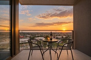 Un balcón con dos sillas y una mesa, con vista a un paisaje urbano al atardecer.
